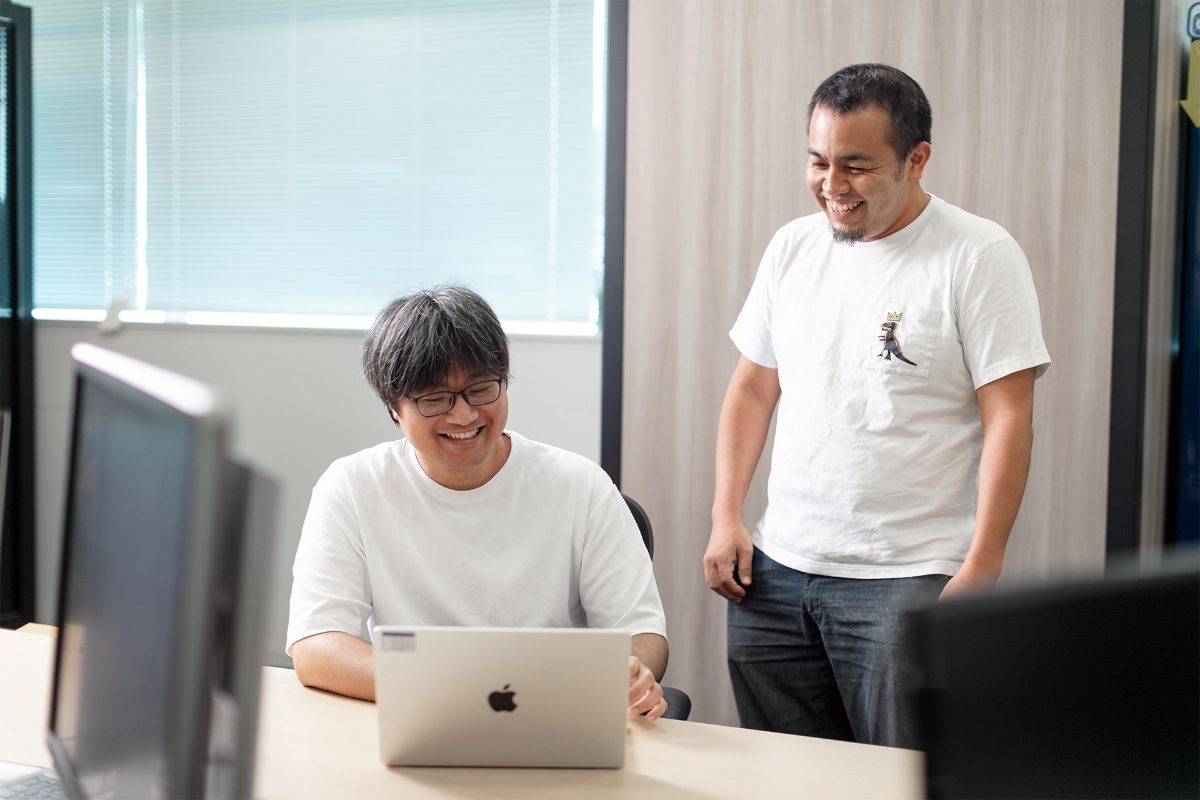 ノートPCを見ながら笑顔で会話するWebエンジニア2名
